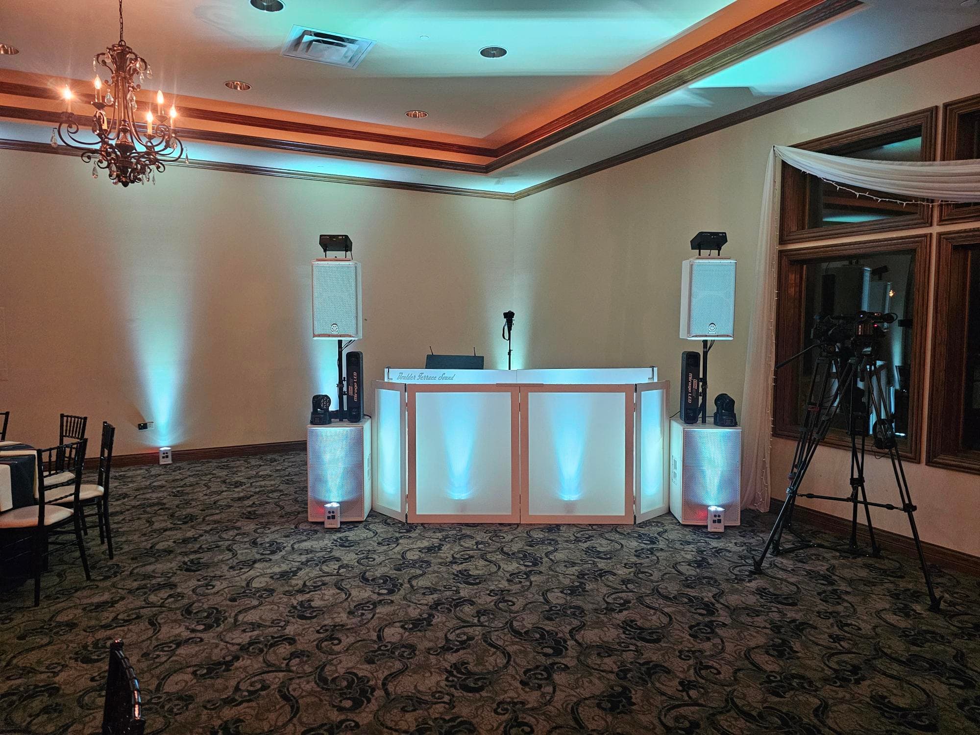 Elegant white DJ booth, speakers, and turquoise uplighting at a wedding reception