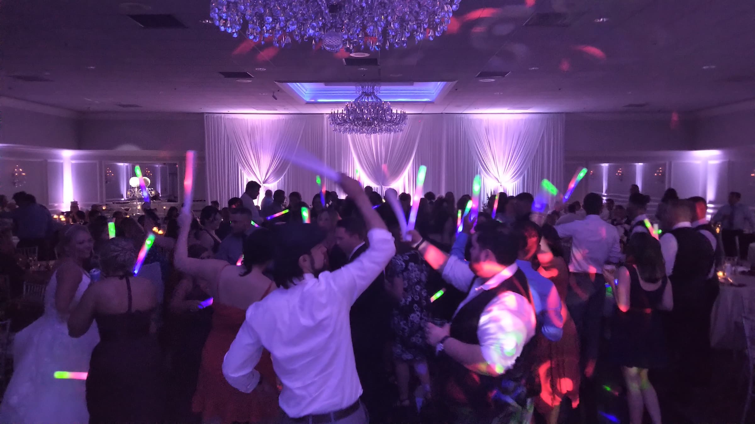 Packed wedding dance floor with guests celebrating under colorful glow-stick lighting