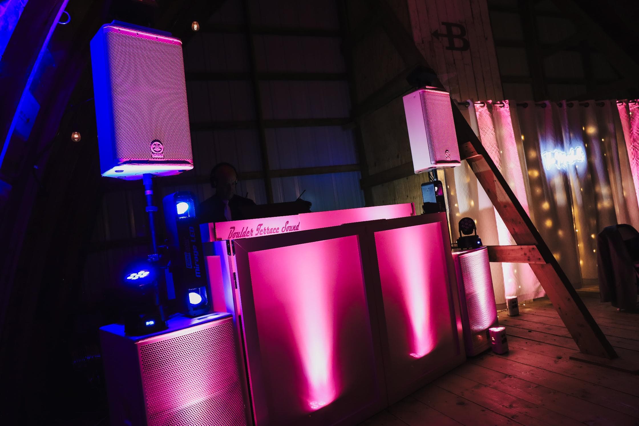 Boulder Terrace Sound DJ booth illuminated in pink and blue at a barn wedding